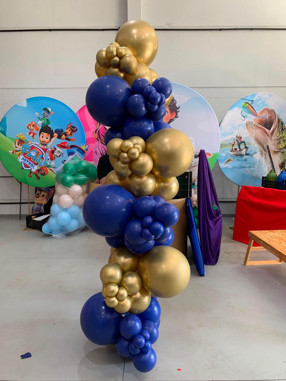 Coluna de balões orgânicos azul marinho e dourado cromado com painéis redondos temáticos ao fundo