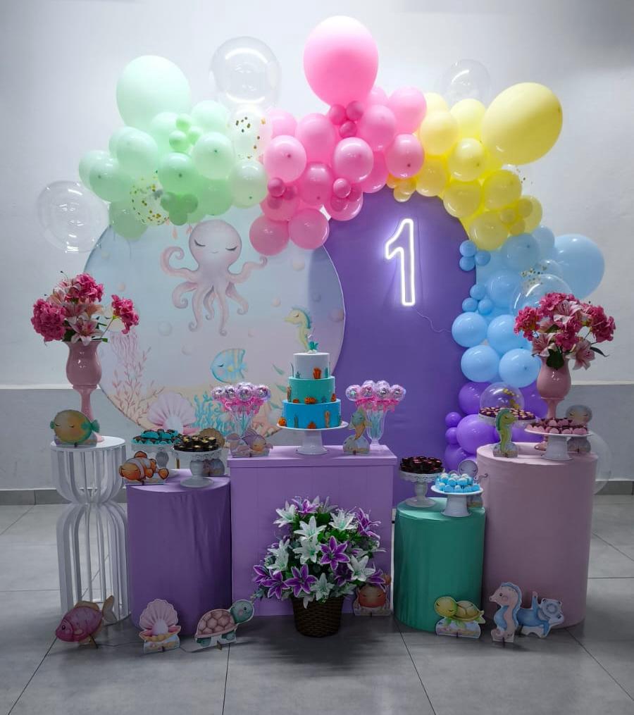 Kit montado no tema Fundo do Mar, com arco orgânico de balões coloridos, painel de polvo e peixes, bolo azul em camadas, neon número 1 e flores — decoração infantil