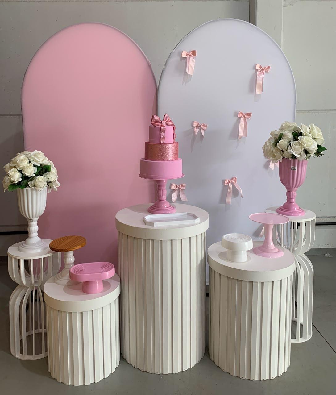 Decoração em tons de rosa e branco com painéis arqueados, laços de cetim, bolo rosa e cilindros ripados