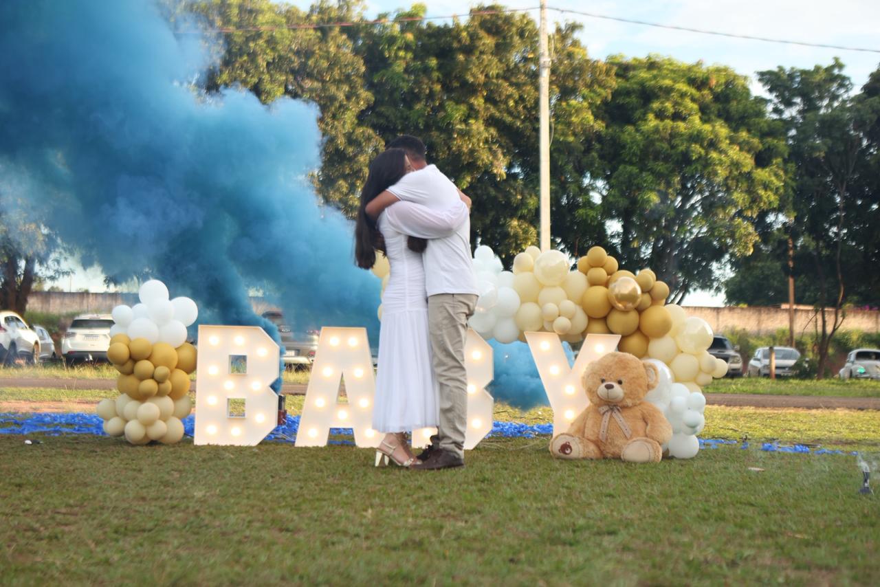 Chá revelação ao ar livre com letras luminosas BABY, fumaça azul, arco de balões dourados e urso de pelúcia