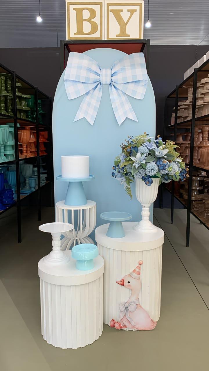 Decoração de chá de bebê menino com painel azul, laço xadrez, cilindros ripados brancos e arranjo de flores azuis