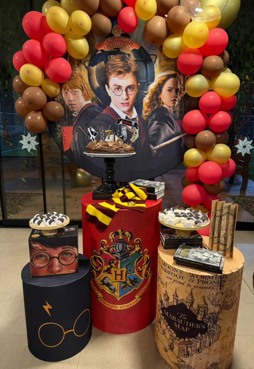 Festa infantil tema Harry Potter com painel Hogwarts Express, arco de balões vermelho e dourado e cilindros temáticos
